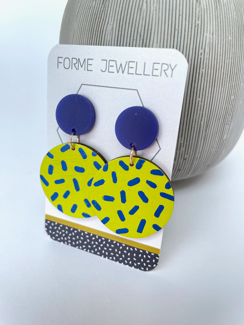 Bright acid yellow circular earrings with a dark blue dash patter
